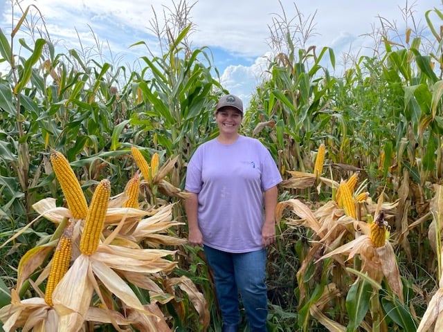 Woman in corn field showing Hybrid85 corn ears